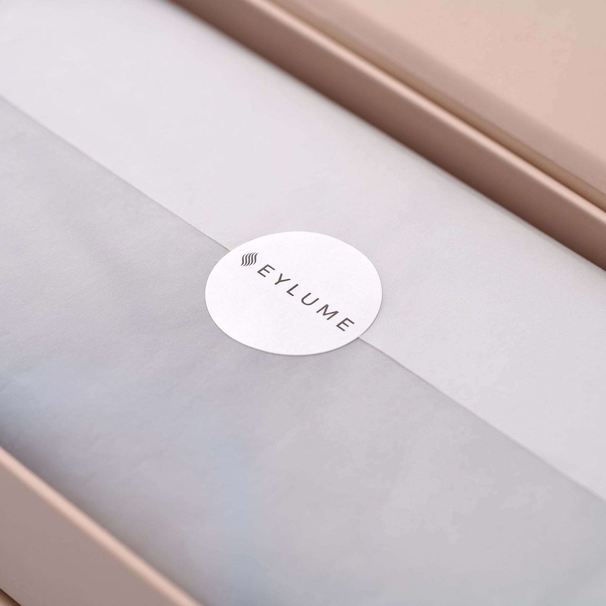 Close-up of the EYLUME Calm Heated Eye Mask packaging, showing the elegant tissue wrap sealed with a branded EYLUME sticker inside the premium gift box