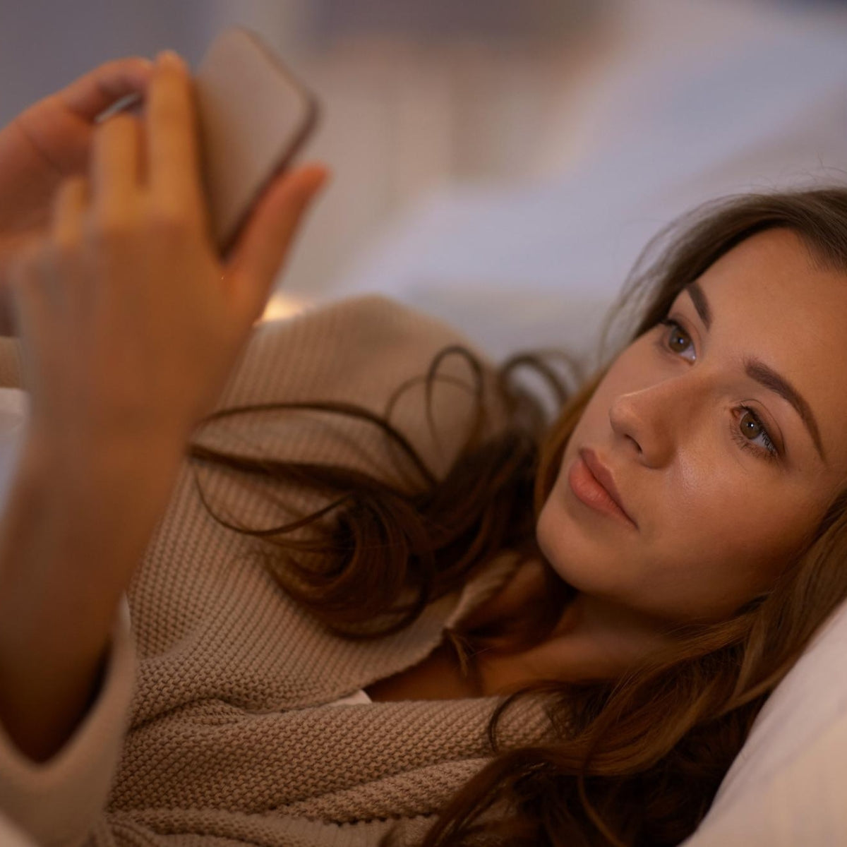 Woman lying on a bed looking at her phone, representing digital eye strain and fatigue caused by prolonged screen use — visual for EYLUME’s “Modern Eyes Are Suffering” section.