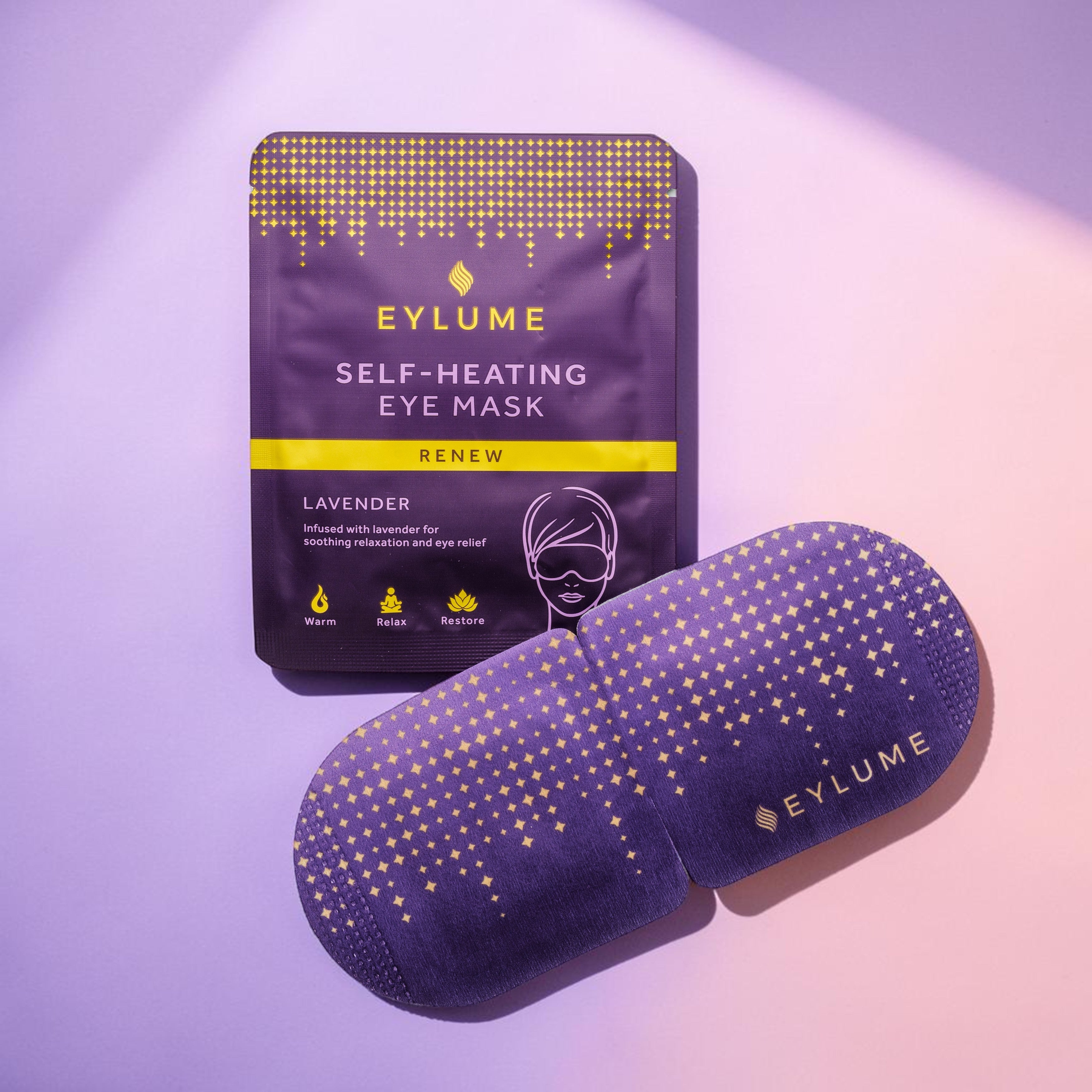 EYLUME Renew Lavender Self Heating Eye Mask sachet and warming eye mask displayed on a soft lilac and blush pink studio background. Lavender infused eye mask designed to relax, soothe tired eyes and support moments of calm.