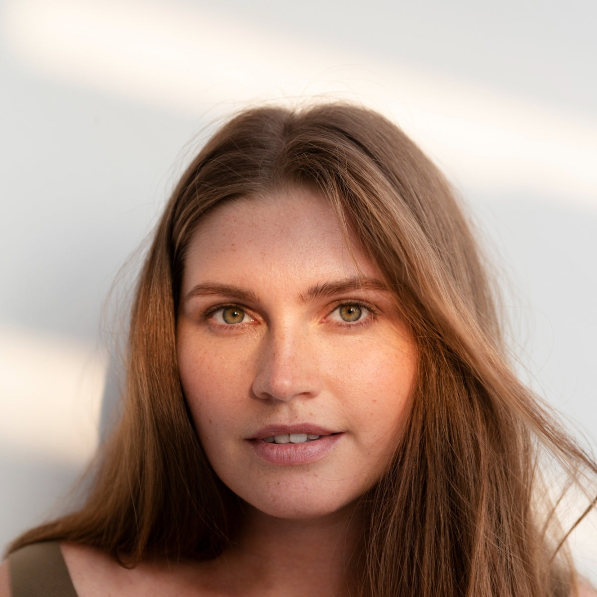 Portrait of a woman with long brown hair smiling softly beside a five-star review for EYLUME’s Calm Heated Eye Mask that reads “Soft, soothing, and instantly relaxing. My tired eyes finally feel alive again.”