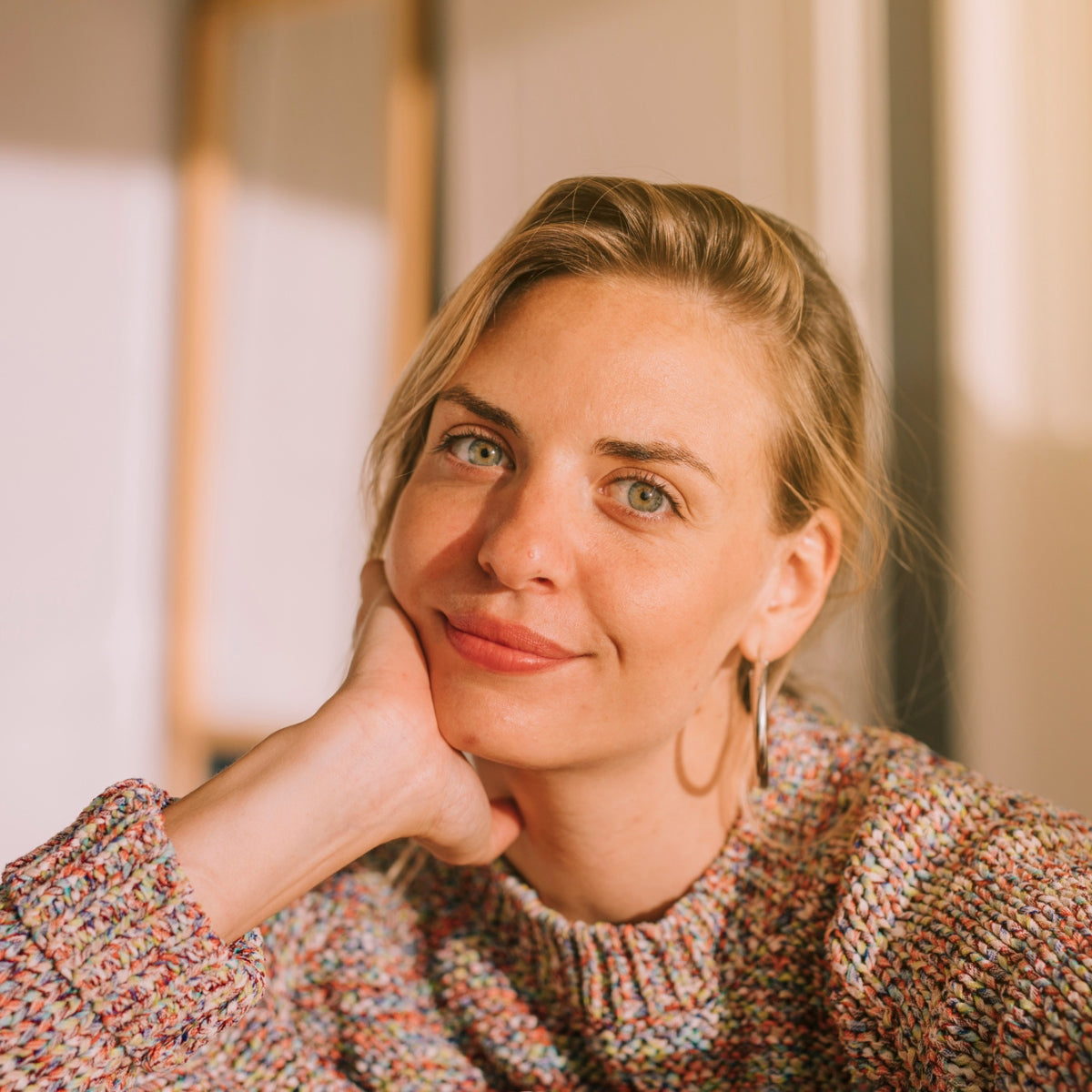 Portrait of a woman with short blonde hair resting her chin on her hand beside a five-star review for EYLUME’s Calm Heated Eye Mask that reads “Gentle comfort, elegant design, and a quiet kind of lasting relief. I love it.”