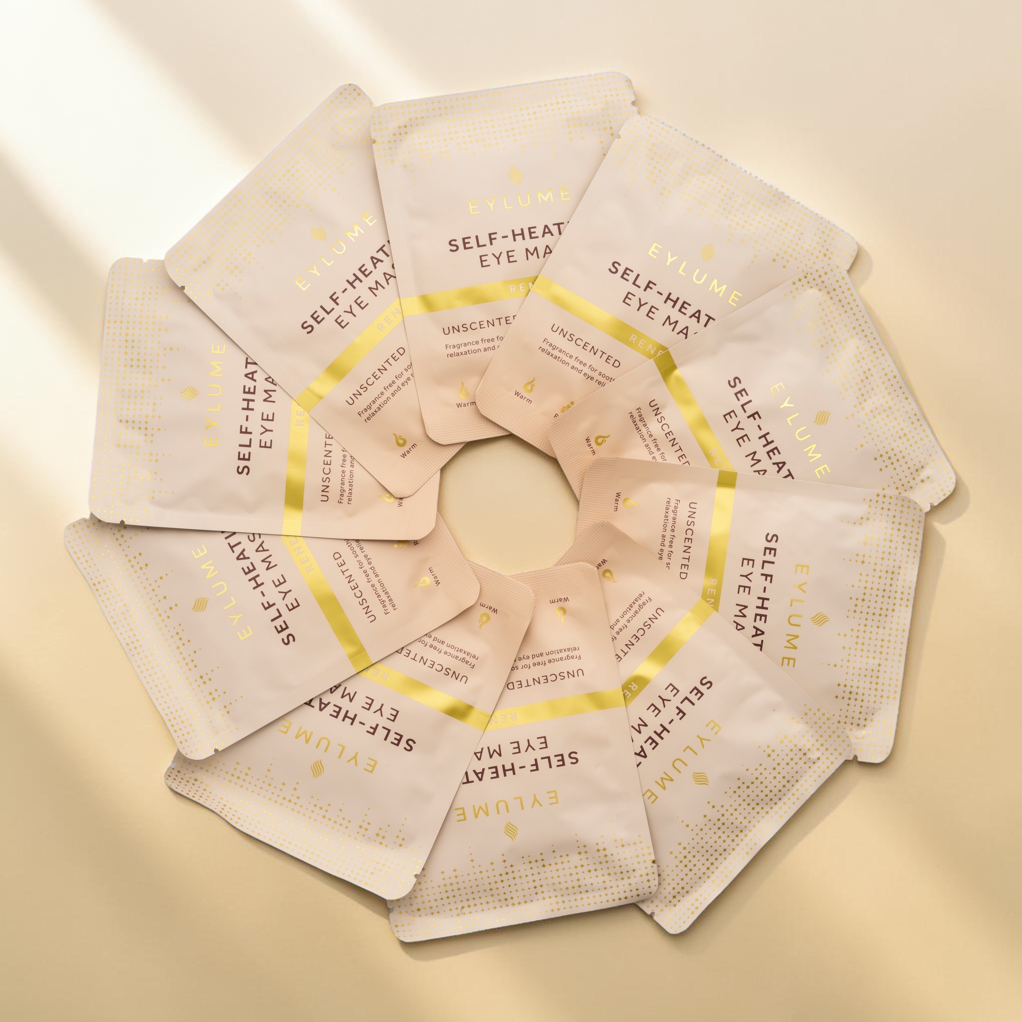 EYLUME RENEW unscented self-heating eye masks arranged in a circular pattern showcasing the fragrance free packaging and single-use masks.